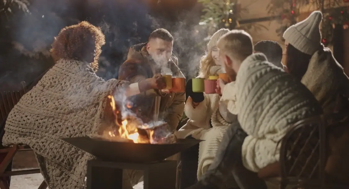 Friends around the fire pit with warm mugs, winter evening