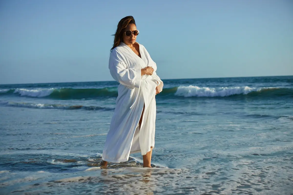 Kim Fields in a white robe at the ocean’s edge